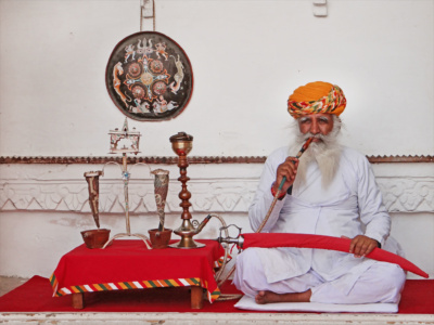 This old Rajput man poses for visitors with a sword on his knees in the palace of Maharaja