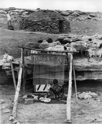 A Native American Navajo woman weaving with a loom
