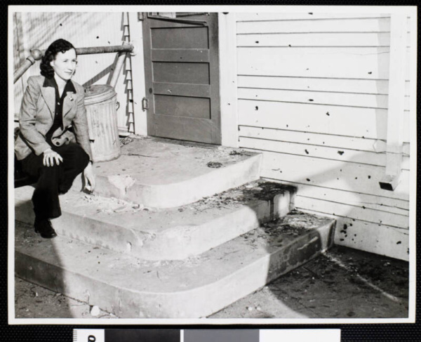 Homeowner Billie Hall poses on flak-riddled back stoop for a newspaper photographer. Feb. 25, 1942