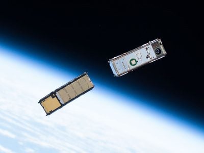 Cropped from original. Original description: A pair of CubeSats, with the Earth's limb in the background, is seen moments after being ejected from a small satellite deployer outside of the space station's Kibo lab module.